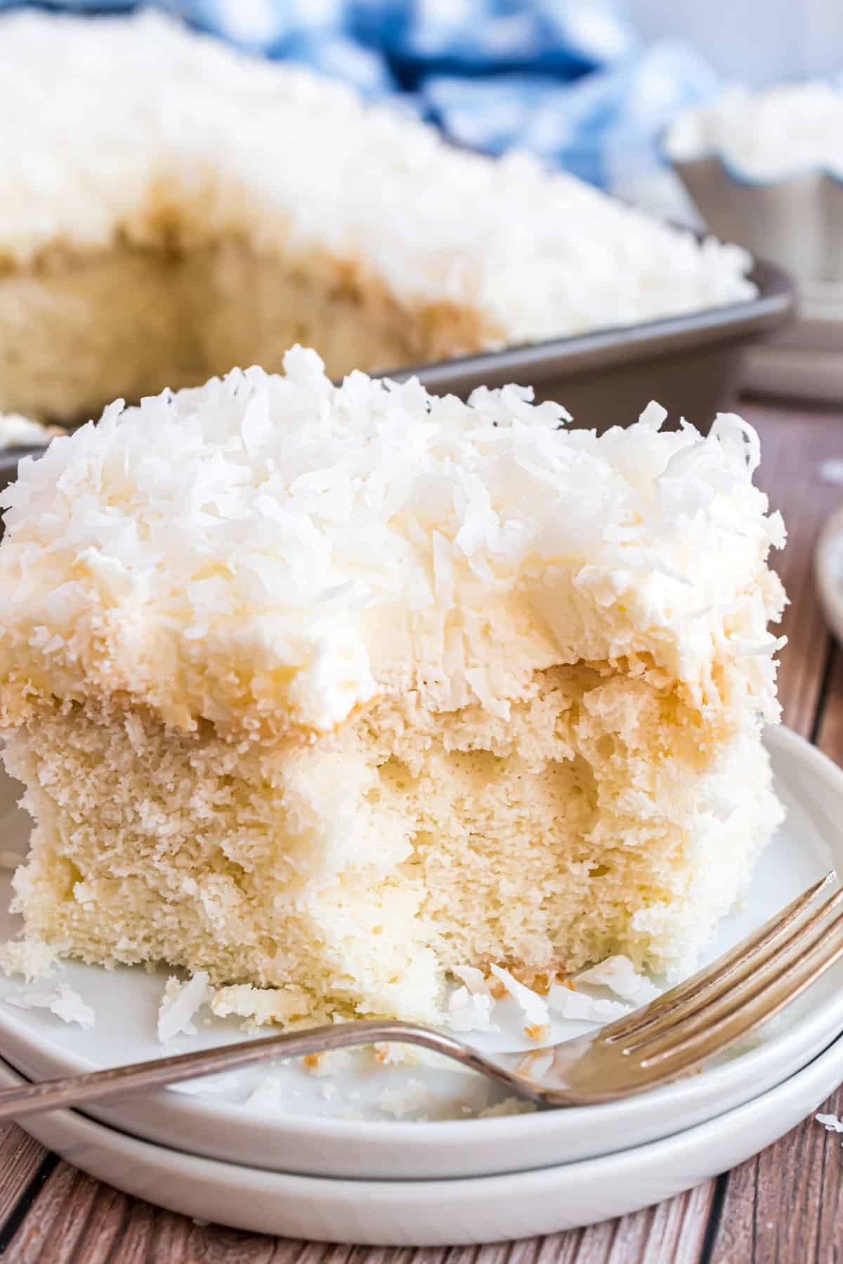 Slice of coconut cake baked in a 13x9 with a bite removed.