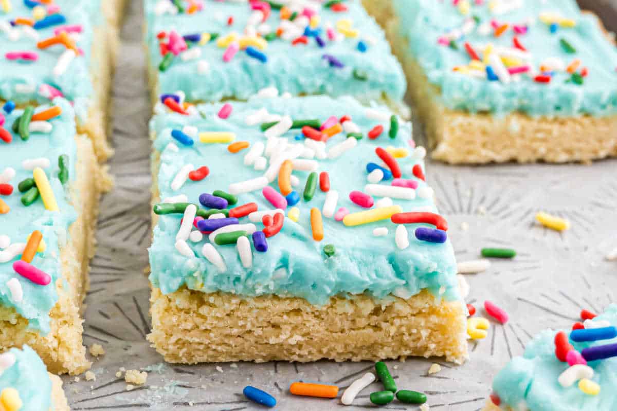 A frosted sugar cookie bar with blue icing and colorful sprinkles, cut into a rectangle—perfect for fans of classic frosted sugar cookie bars.