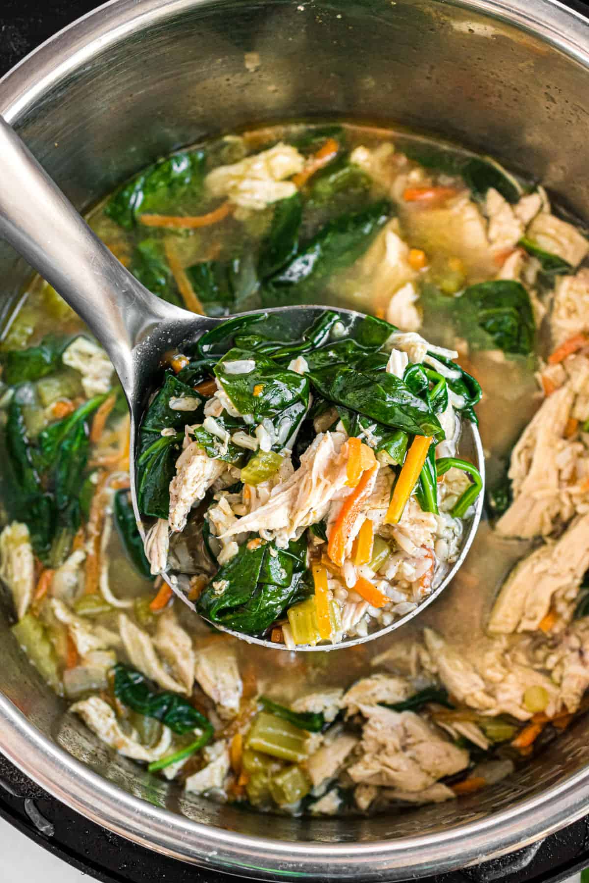 Chicken and rice soup with spinach being ladled out of the pressure cooker.