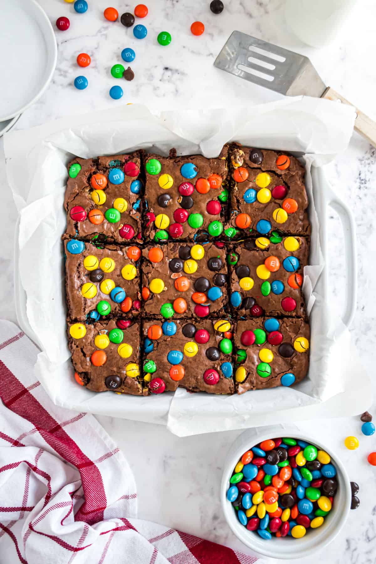 M&Ms brownies in a square baking dish with parchment paper cut into 9 squares.