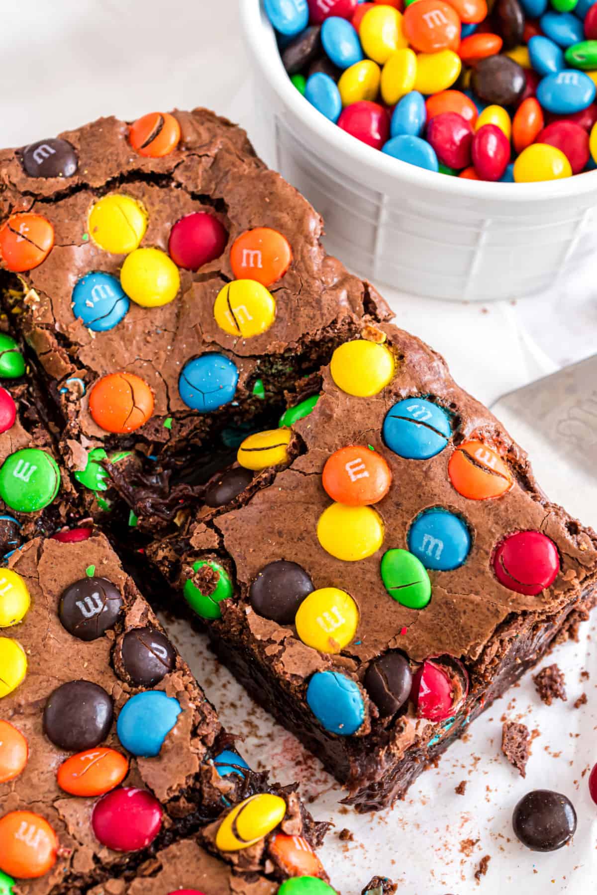 M&M brownies cut into squares with bowl of candies in background.