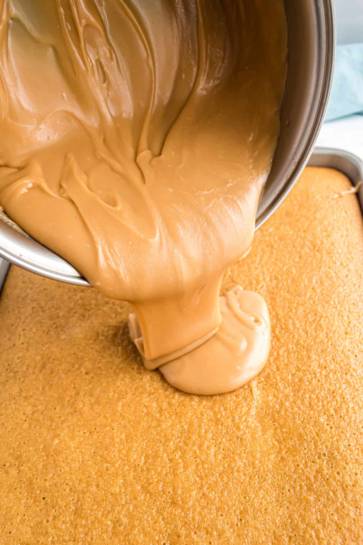 Peanut butter frosting being poured over warm peanut butter sheet cake.