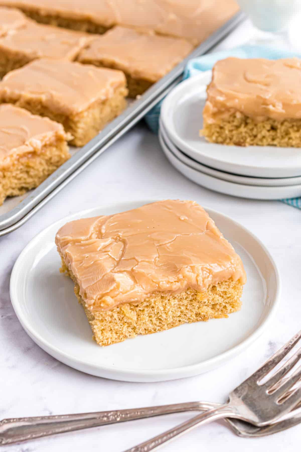 Slice of peanut butter cake on white plate with remaining cake in background.