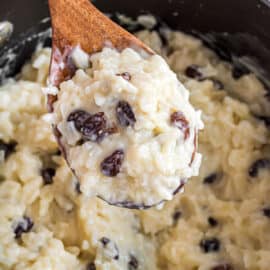 Rice pudding with raisings being spooned out of saucepan.