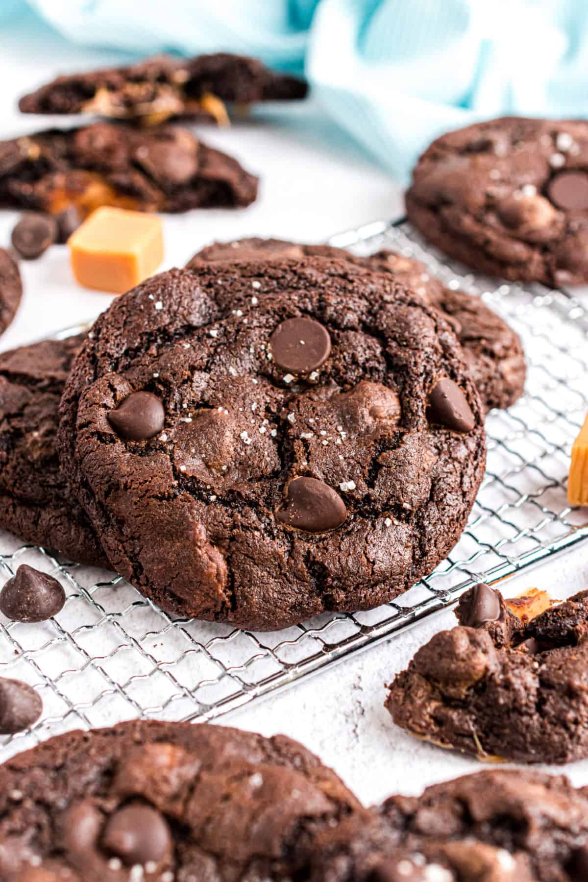 Chocolate cookie on a wire rack with a caramel in background.