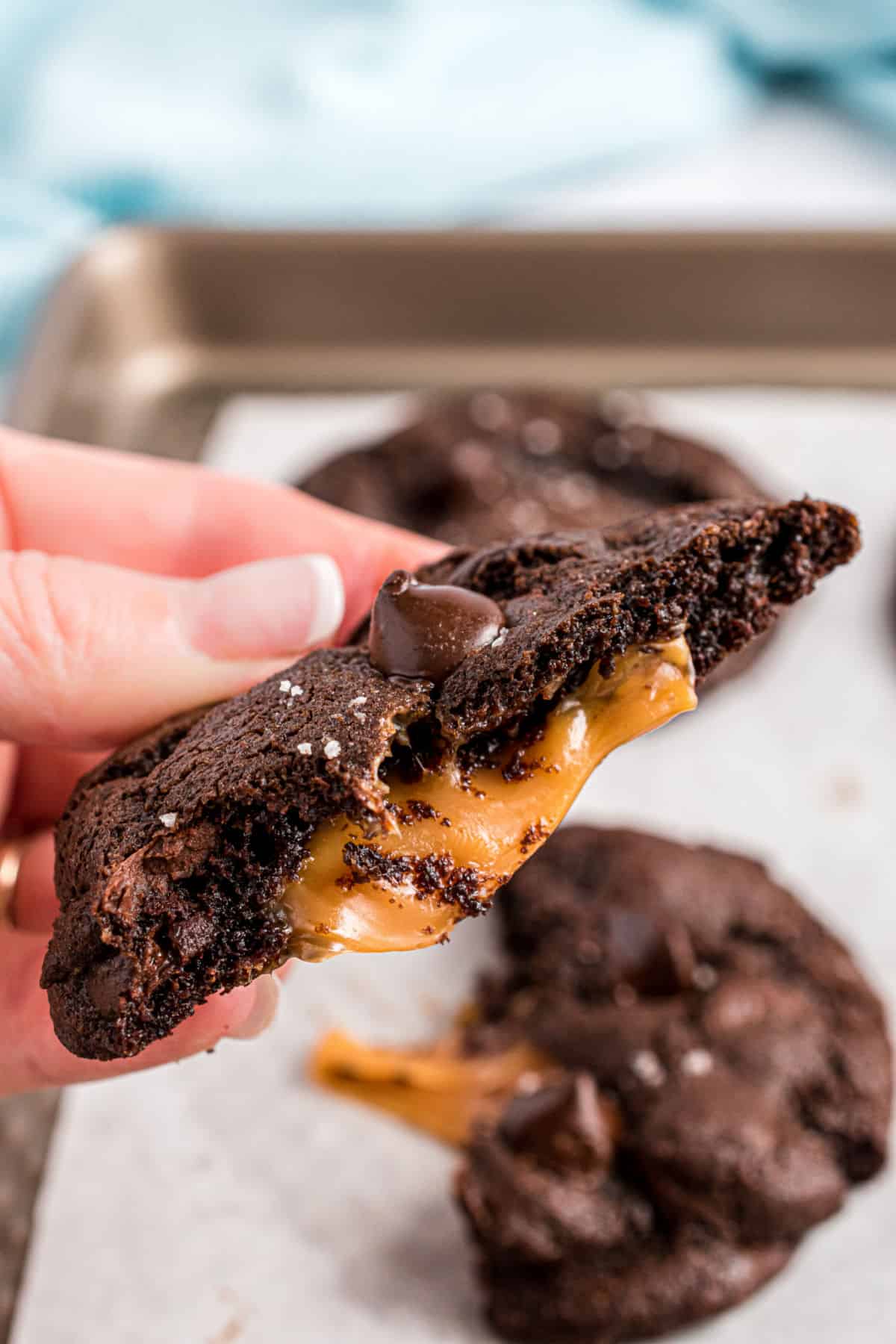 Hand holding a chocolate cookie with caramel oozing out the middle.