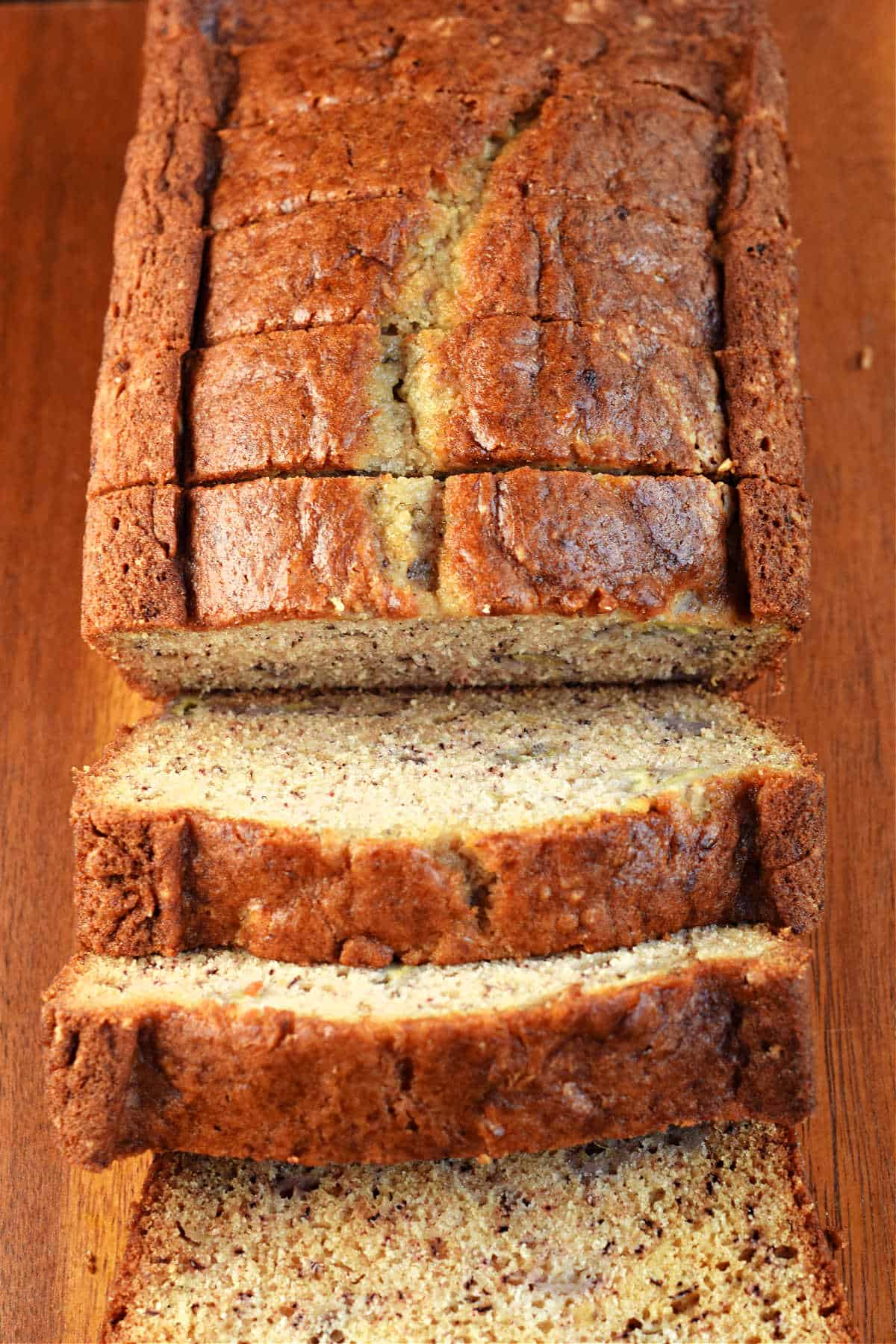 Loaf of banana bread on wooden cutting board with thick slices cut.