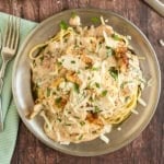 A plate of creamy Italian pasta with grilled chicken, topped with fresh herbs and grated cheese, sits invitingly on a rustic wooden table.