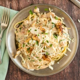 A plate of creamy Italian pasta with grilled chicken, topped with fresh herbs and grated cheese, sits invitingly on a rustic wooden table.