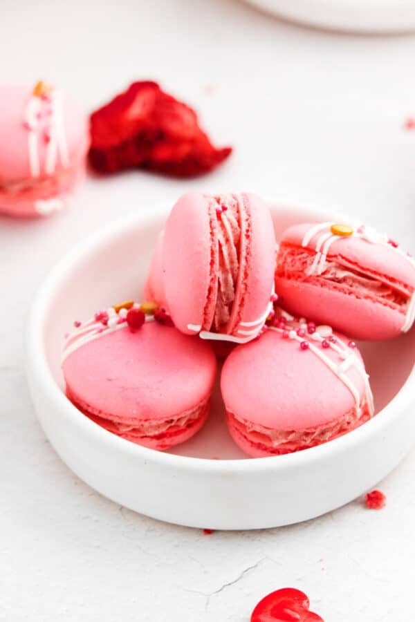Strawberry macarons in a white bowl.