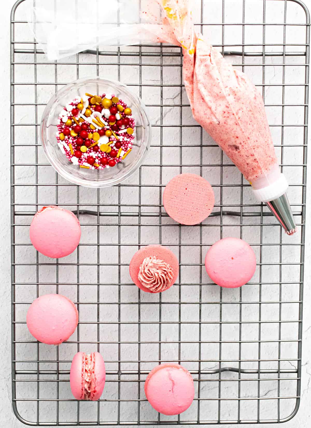 Pink macaron shells being filled with strawberry buttercream.