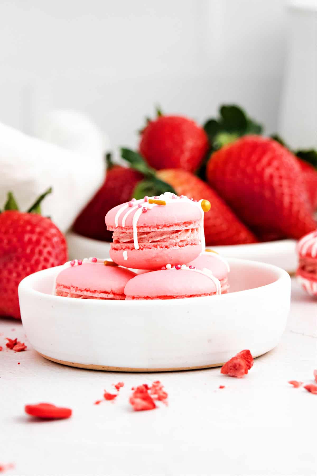 Strawberry macarons in a bowl with fresh strawberries in background.