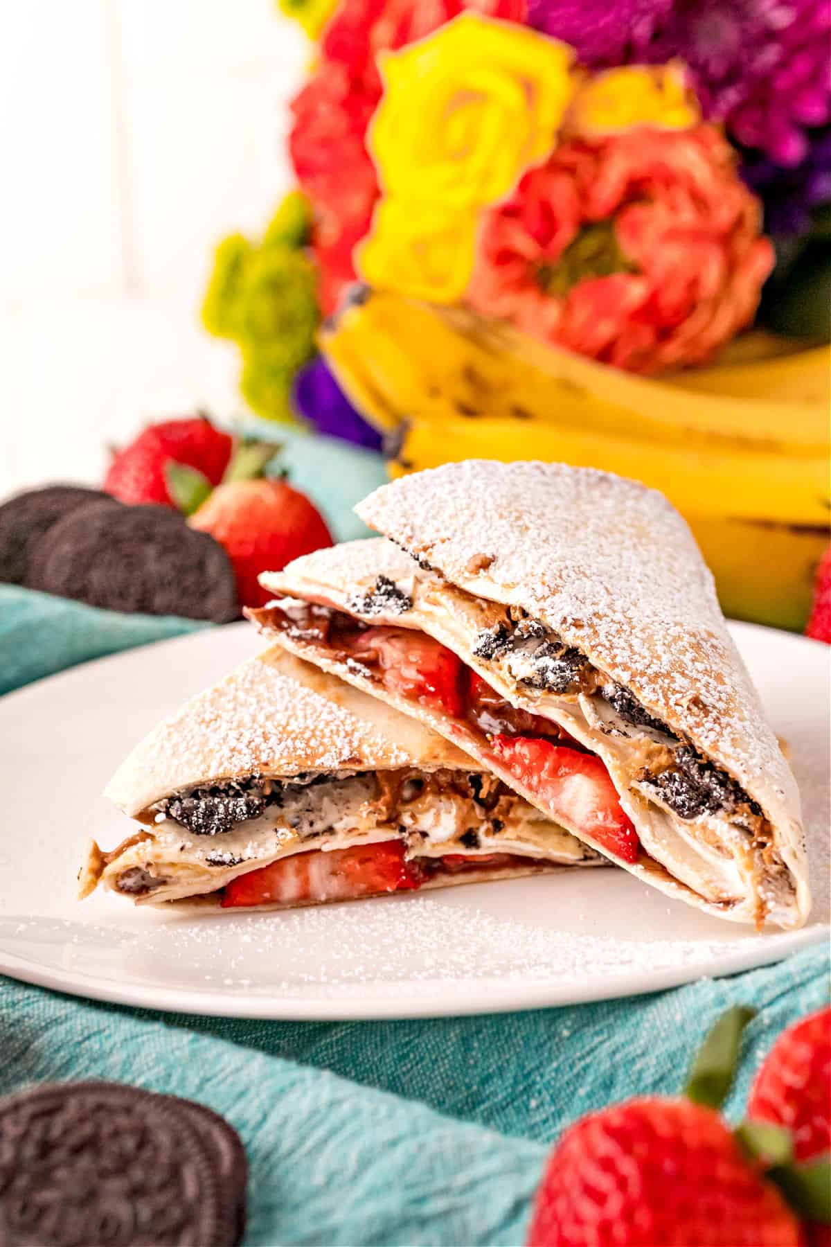 Dessert tortilla wrap on a white plate with colorful flowers in background.