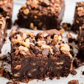 Square of thick, fudgy brownie packed with walnuts on a piece of parchment paper.