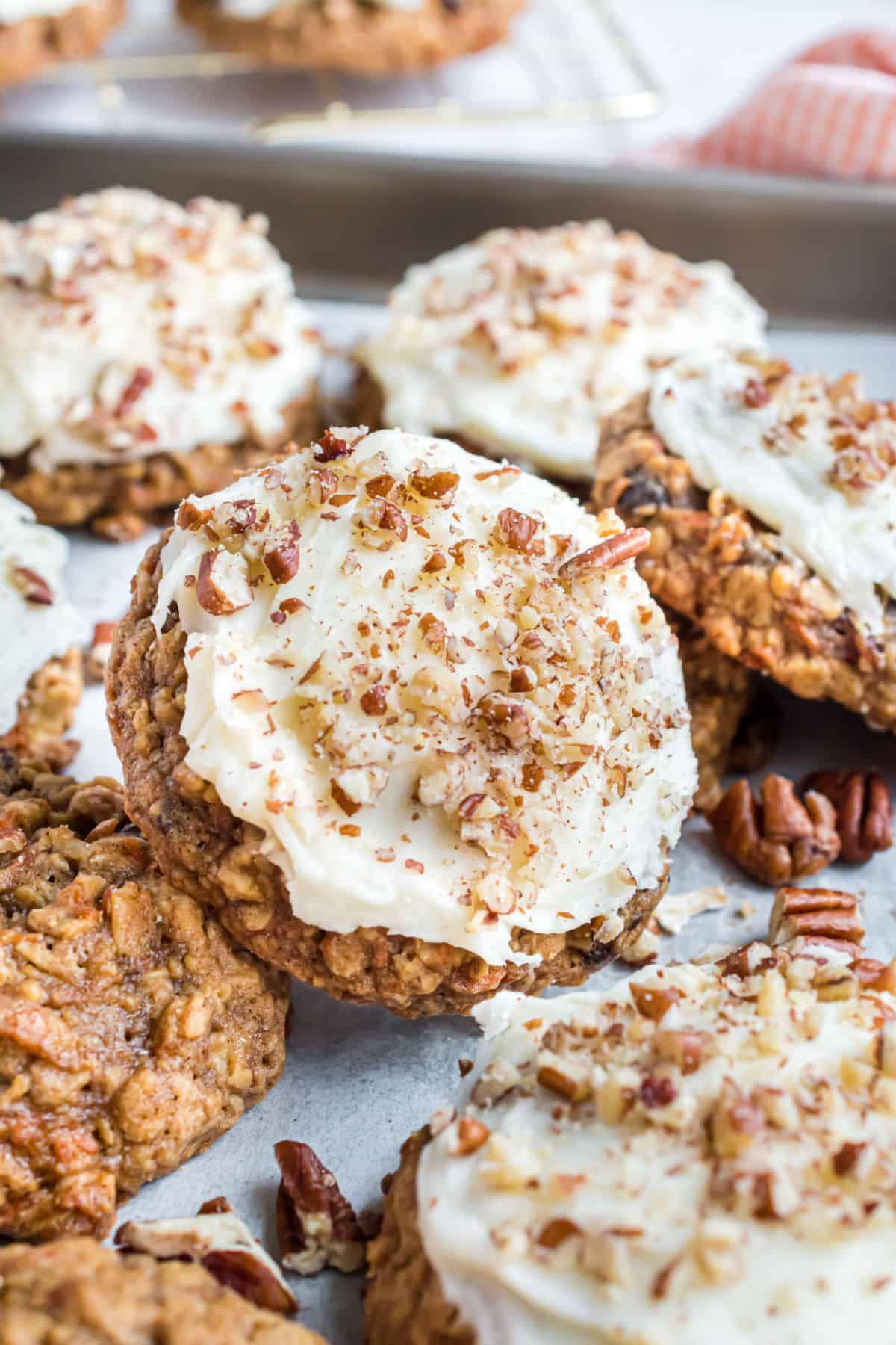 Stack of frosted and unfrosted carrot cake cookies on baking sheet.