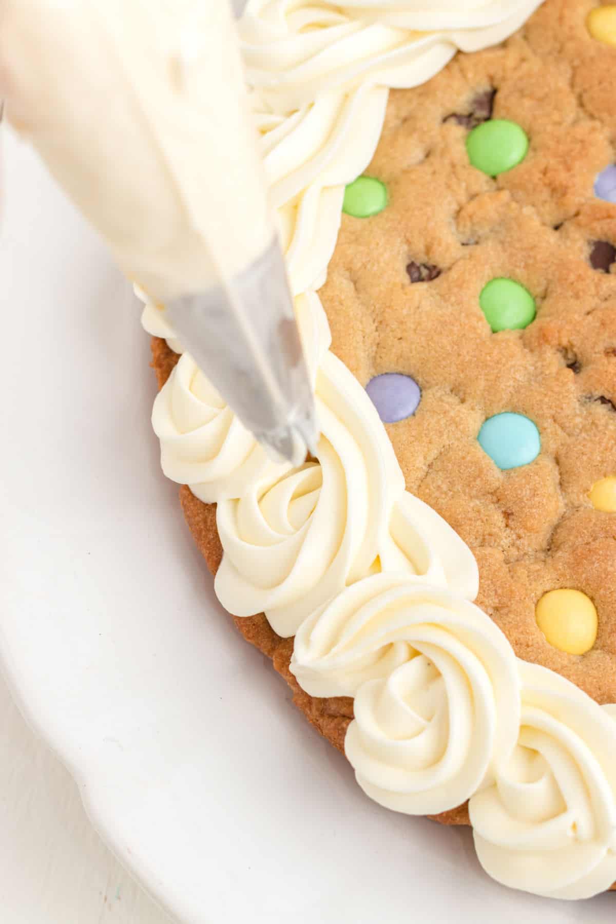 Sugar cookie frosting being piped onto an Easter cookie cake.