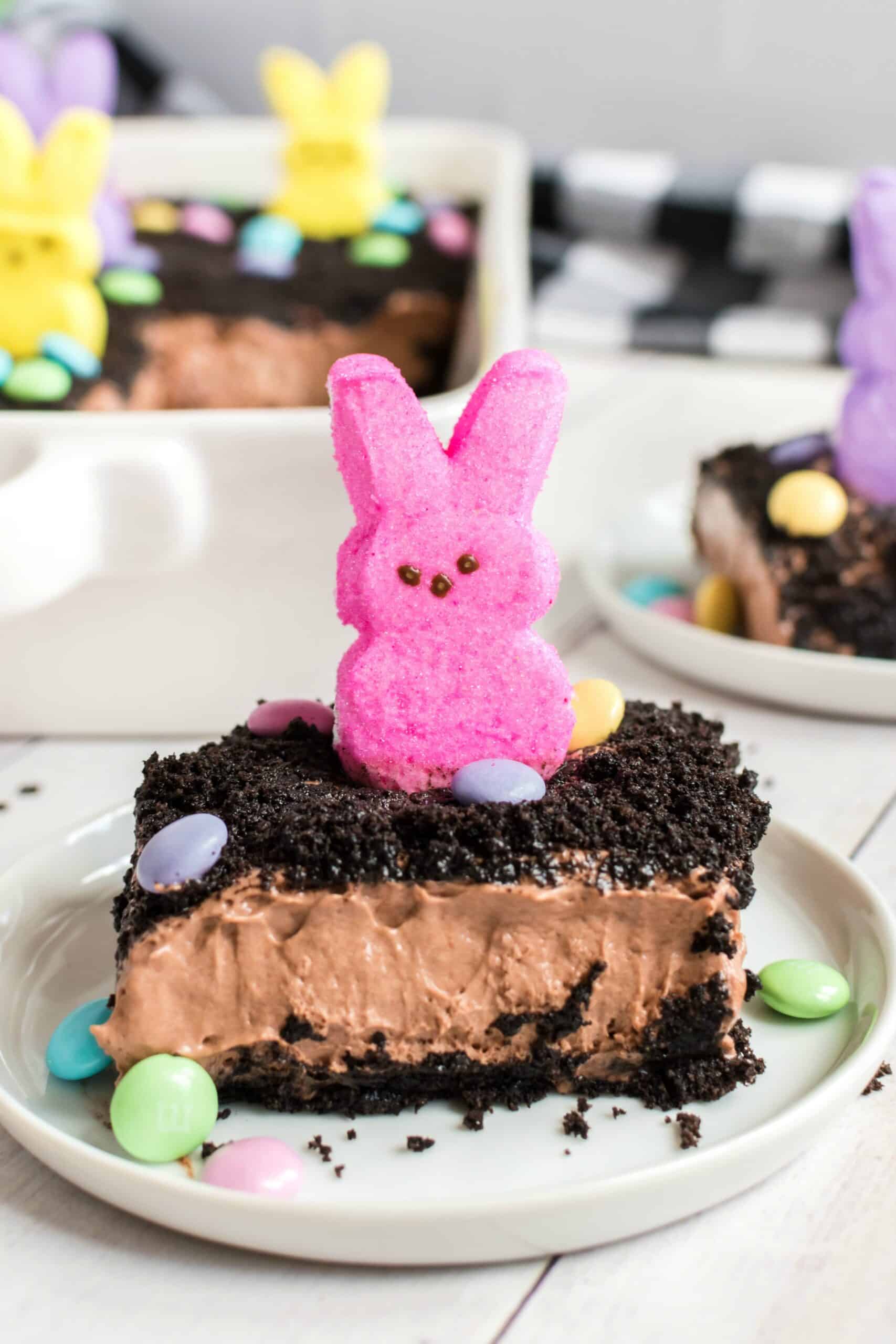 Slice of Easter dirt pudding cake on a white plate, topped with PEEPS.