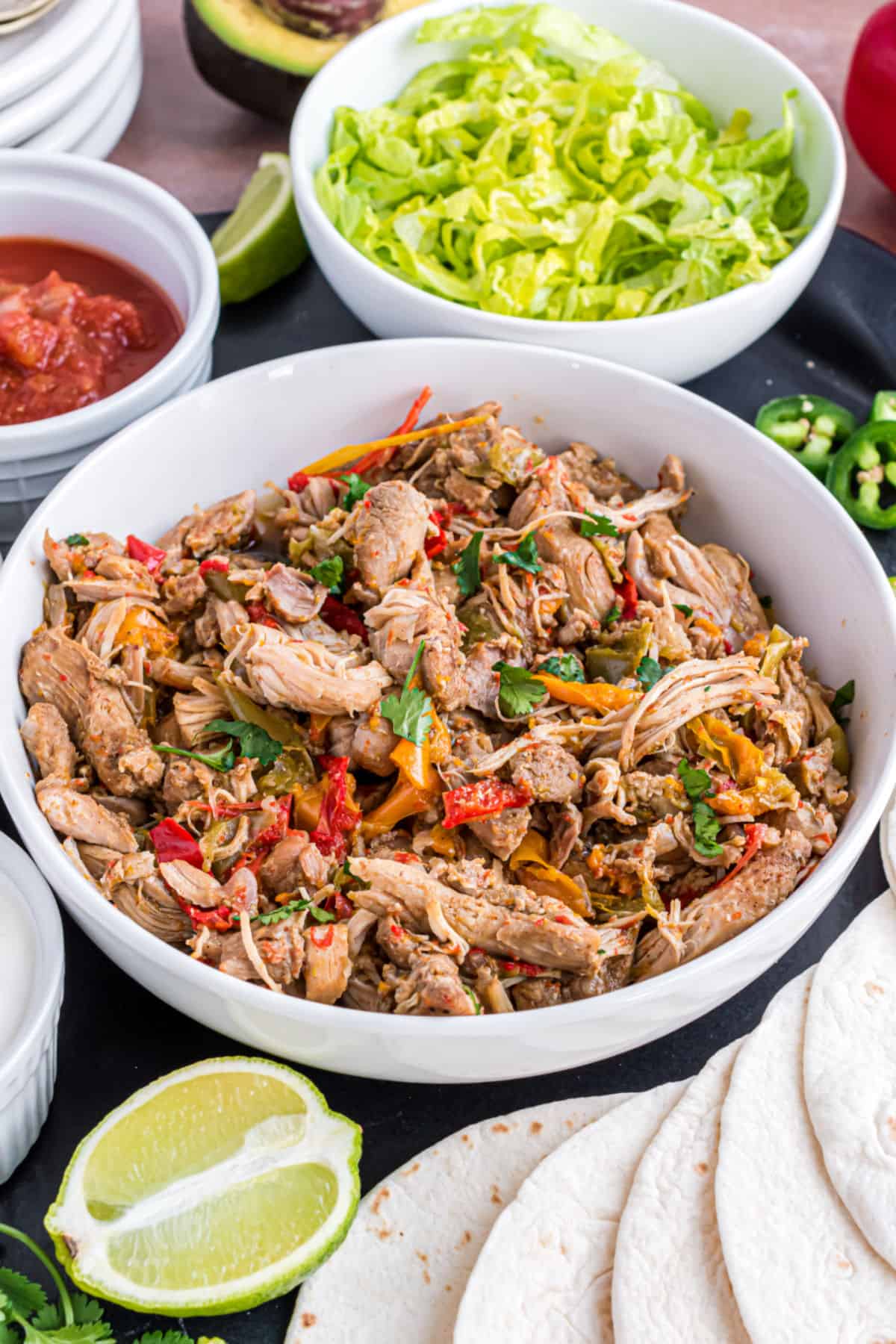 Chicken fajitas in a serving bowl with toppings on the side.