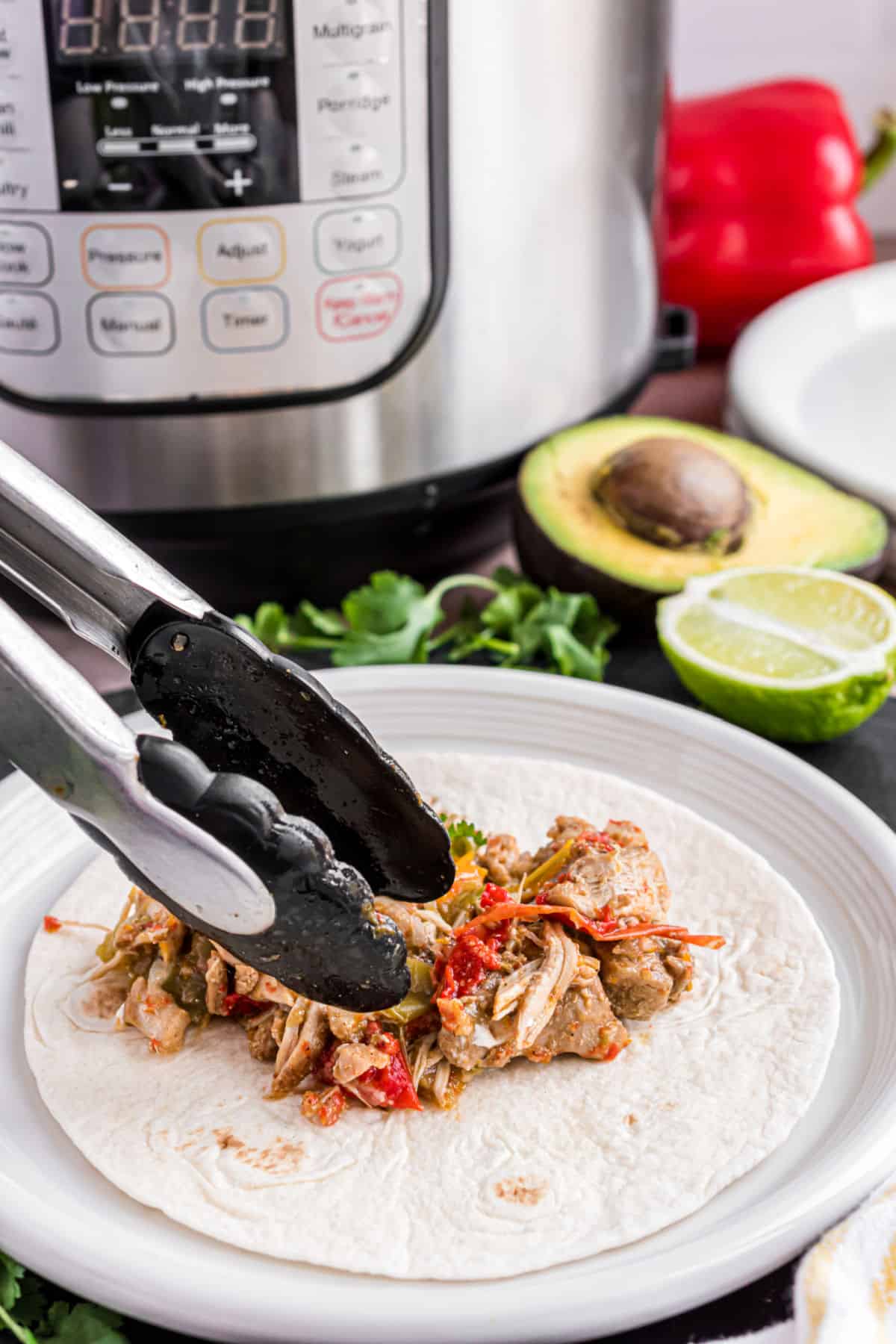 Chicken fajitas made in the Instant Pot being put on a flour tortilla with tongs.