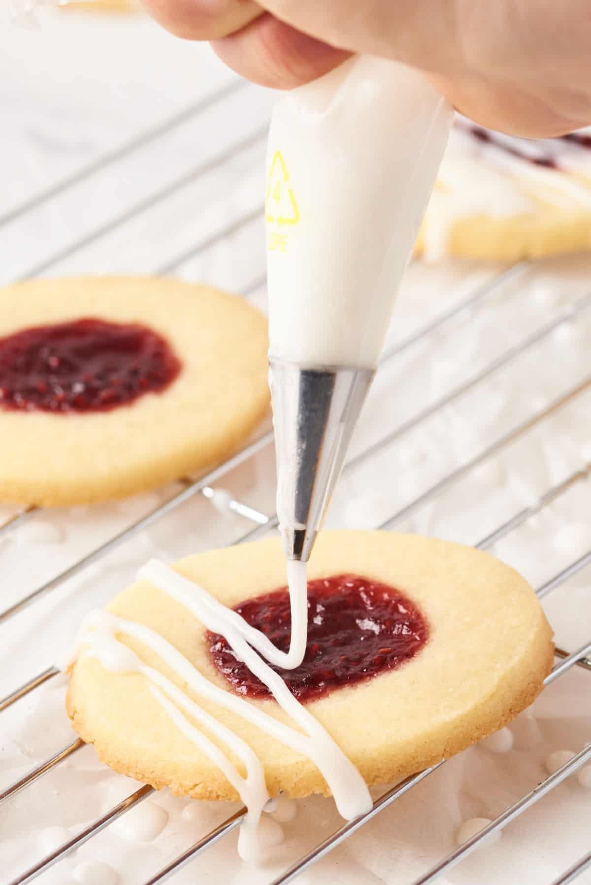 Jam thumbprint cookies being drizzled with icing.