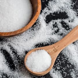 Kosher salt in a wooden bowl spilled onto a balck surface with a wooden spoon.