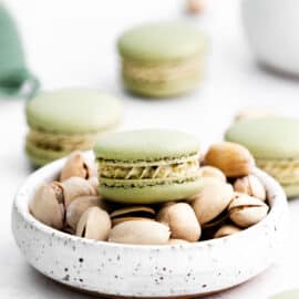 Pistachio macarons on a bowl of pistachios.