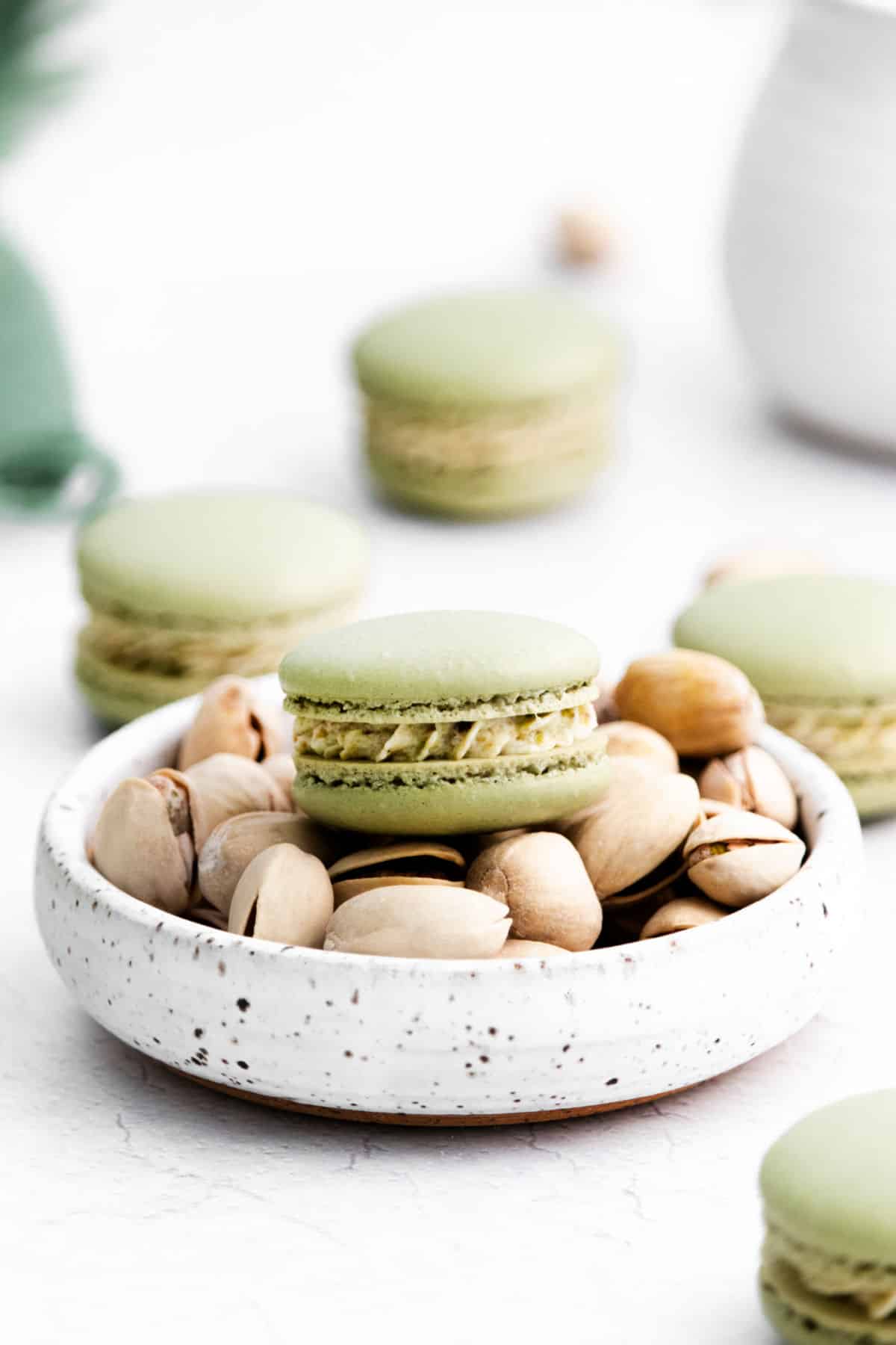 Pistachio macarons on a bowl of pistachios.