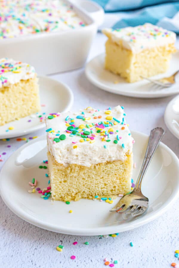 Slices of vanilla cake with vanilla frosting and sprinkles on small plates.