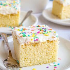 Slice of vanilla cake with vanilla frosting and colorful sprinkles.