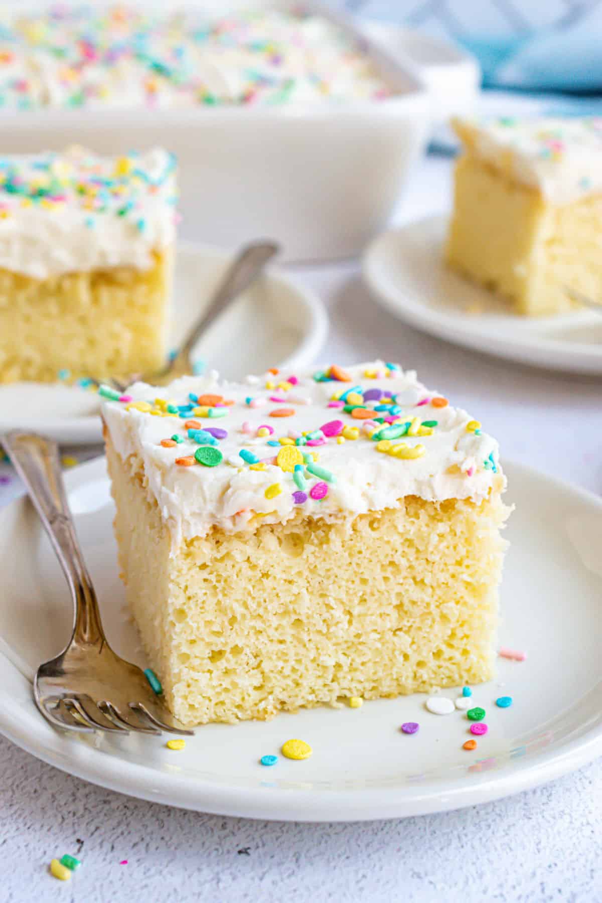 Slice of vanilla cake with vanilla frosting and colorful sprinkles.