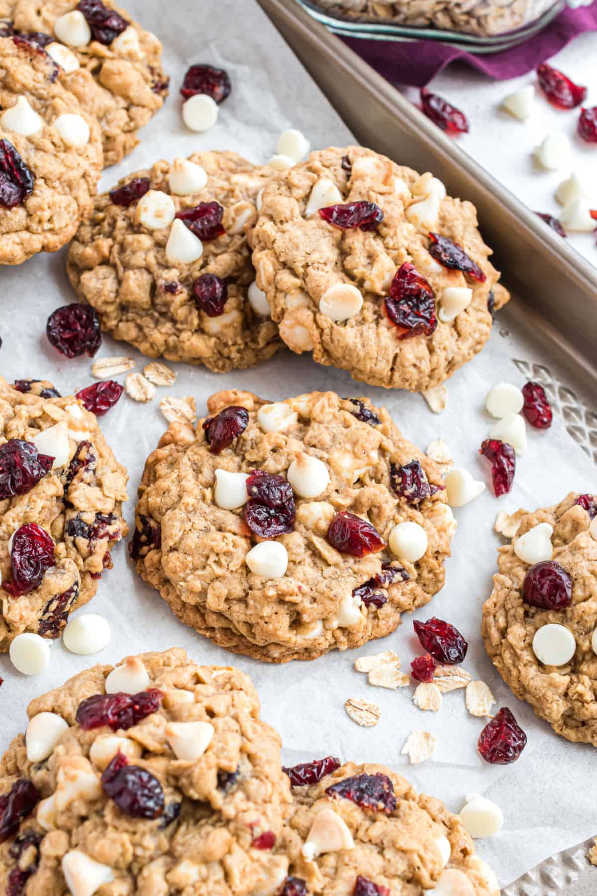 Stacks of white chocolate oatmeal cranberry cookies on a parchment paper lined cookie sheet.