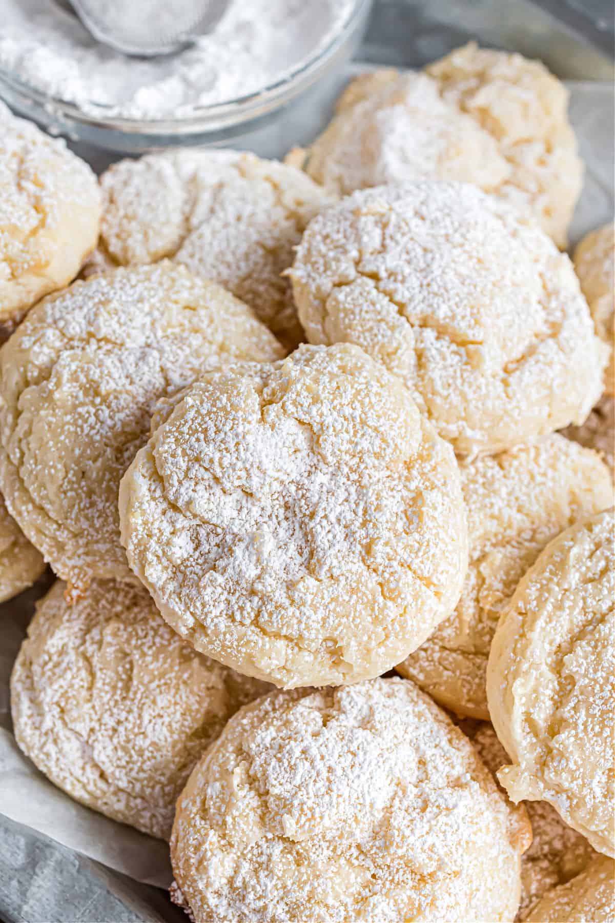 Cheesecake cookies topped with powdered sugar and stacked on a plate.