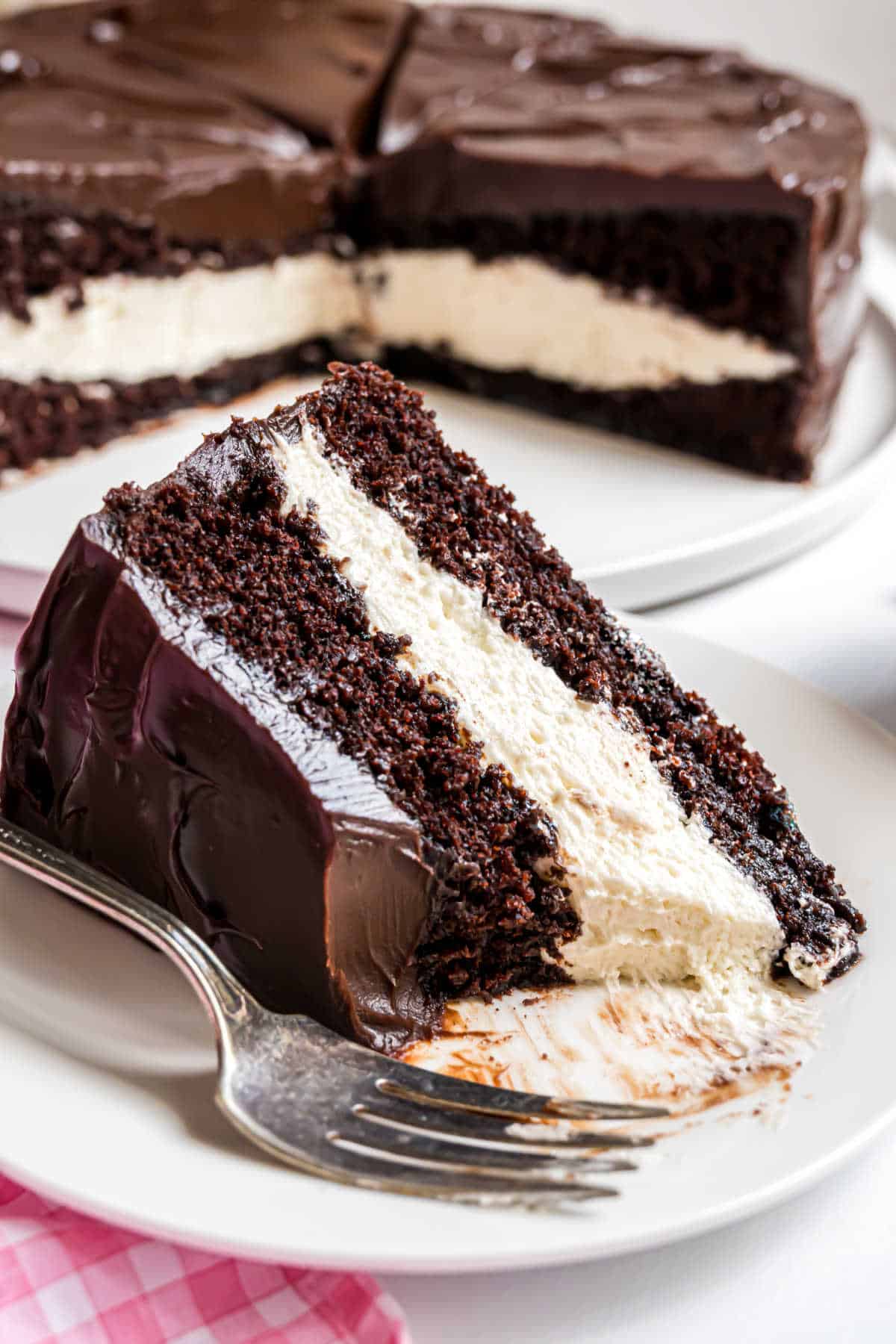 A slice of ding dong cake with white cream filling and rich chocolate frosting sits on a white plate with a fork.
