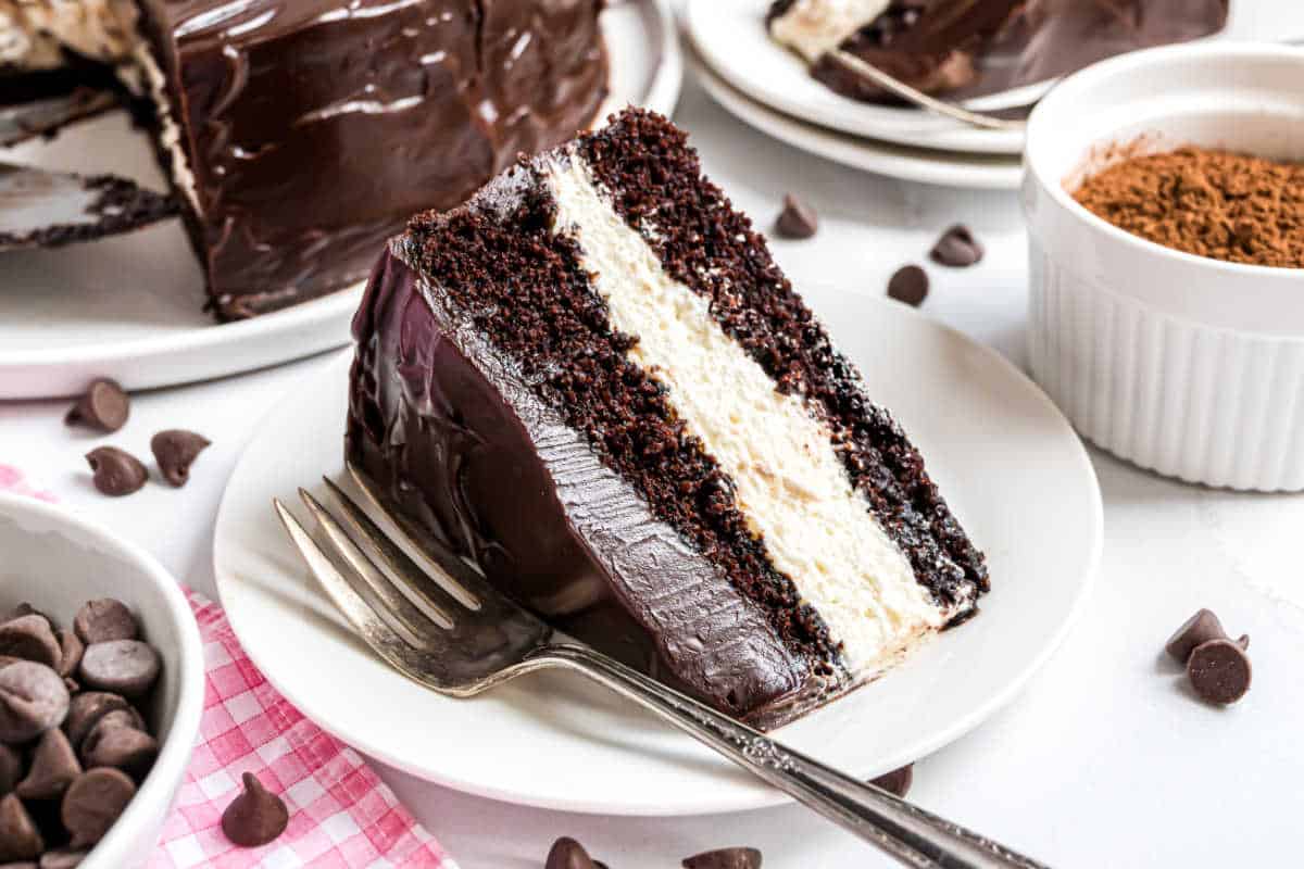 A slice of decadent ding dong cake with cream layers and rich chocolate ganache sits on a white plate with a fork.