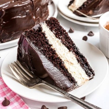 A slice of rich ding dong cake with white cream filling and chocolate frosting sits on a white plate with a fork.