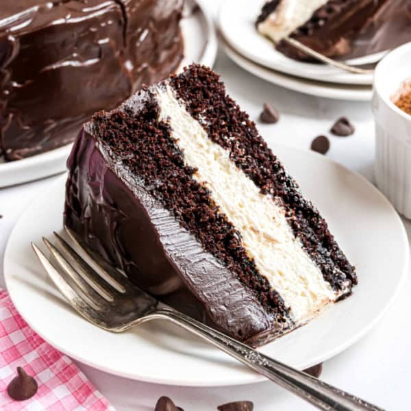 A slice of rich ding dong cake with white cream filling and chocolate frosting sits on a white plate with a fork.