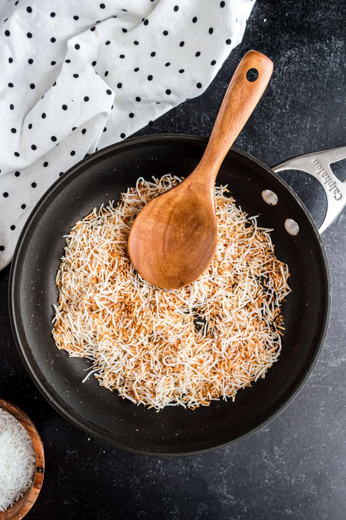 Toasted coconut in a skillet with wooden spoon.