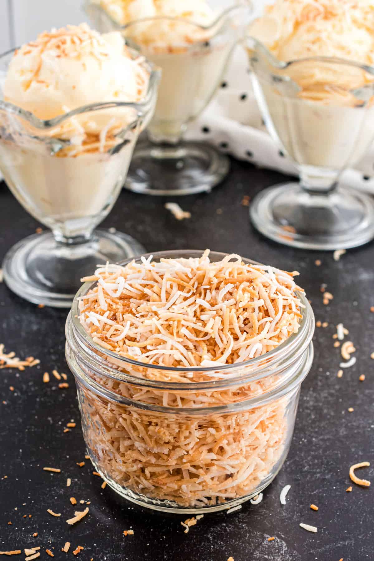 Toasted coconut in a small jar with ice cream in background.
