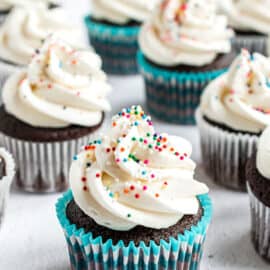 Vanilla buttercream frosting piped onto chocolate cupcakes with sprinkles.