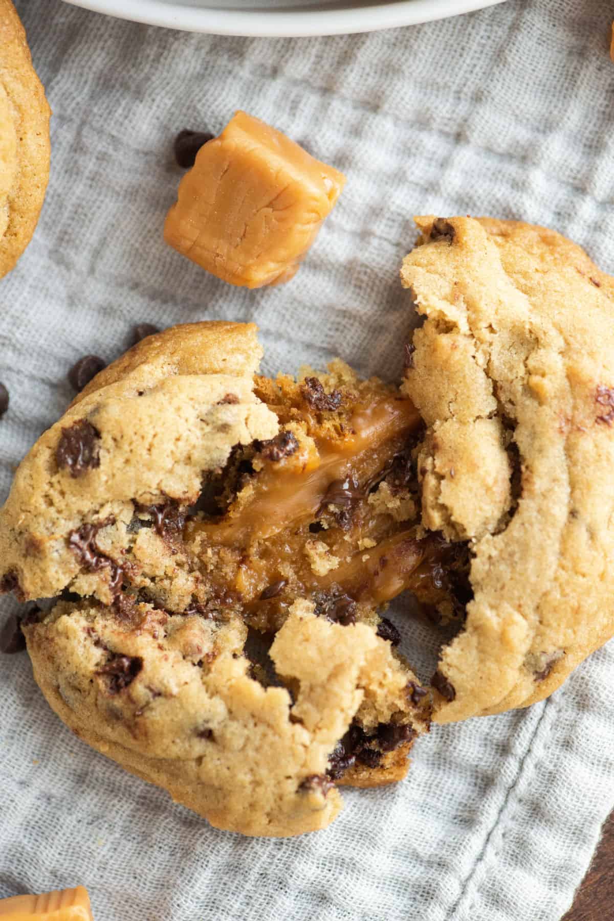 Caramel stuffed chocolate chip cookie broken in half to reveal gooey caramel center.