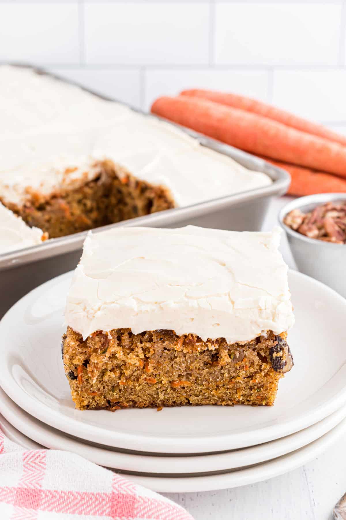 Slice of carrot cake on a white plate with 13x9 in background.