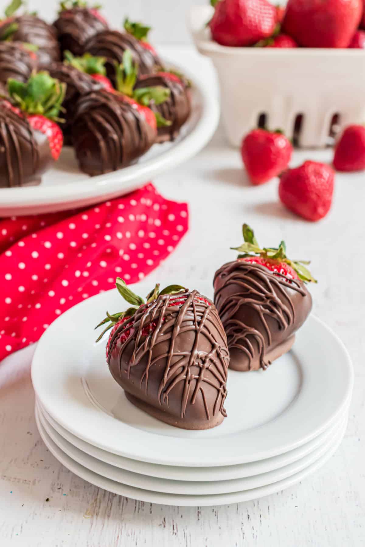 Chocolate dipped strawberries on a stack of white dessert plates.