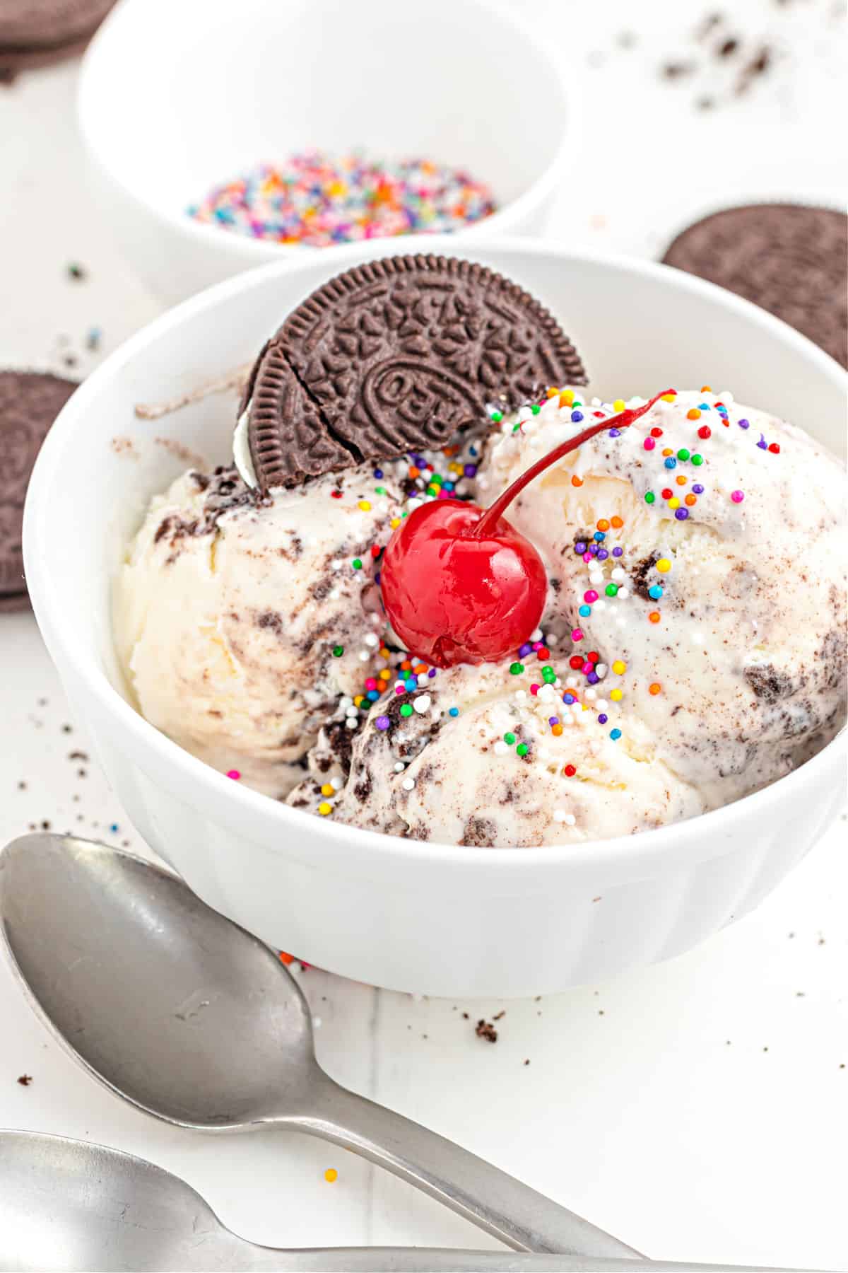 Oreo ice cream sundae in a white bowl with sprinkles and cherry.