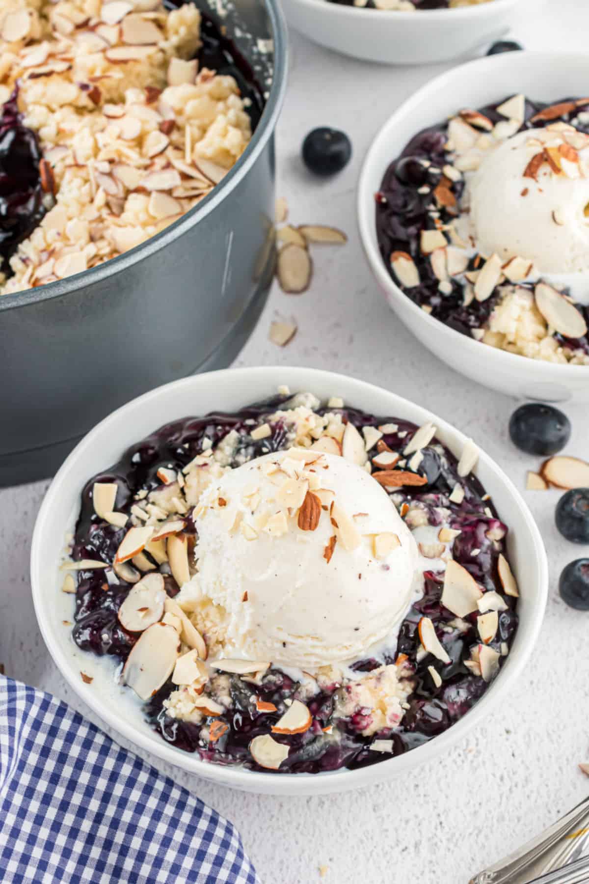 Blueberry cobbler with sliced almonds in white bowls with vanilla ice cream on top.