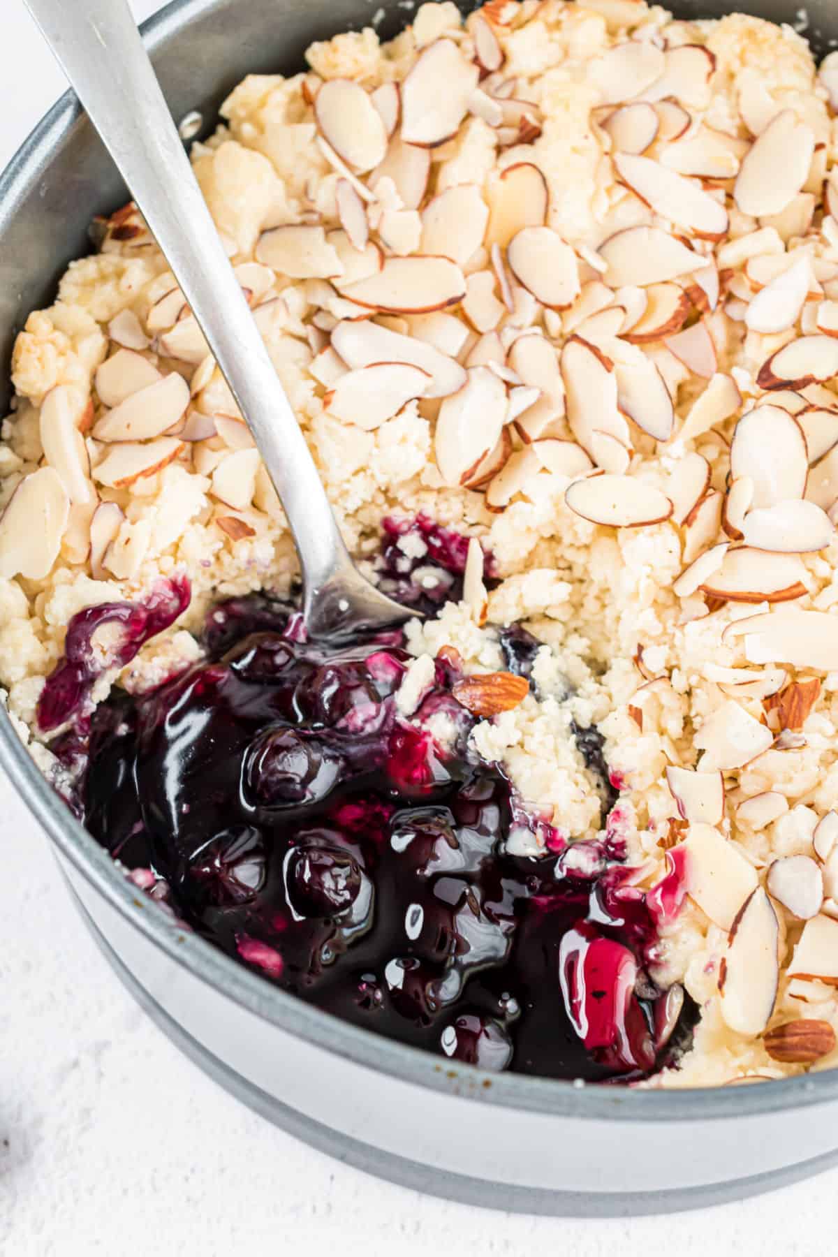 Spoon of blueberry cobbler being lifted out of pan.