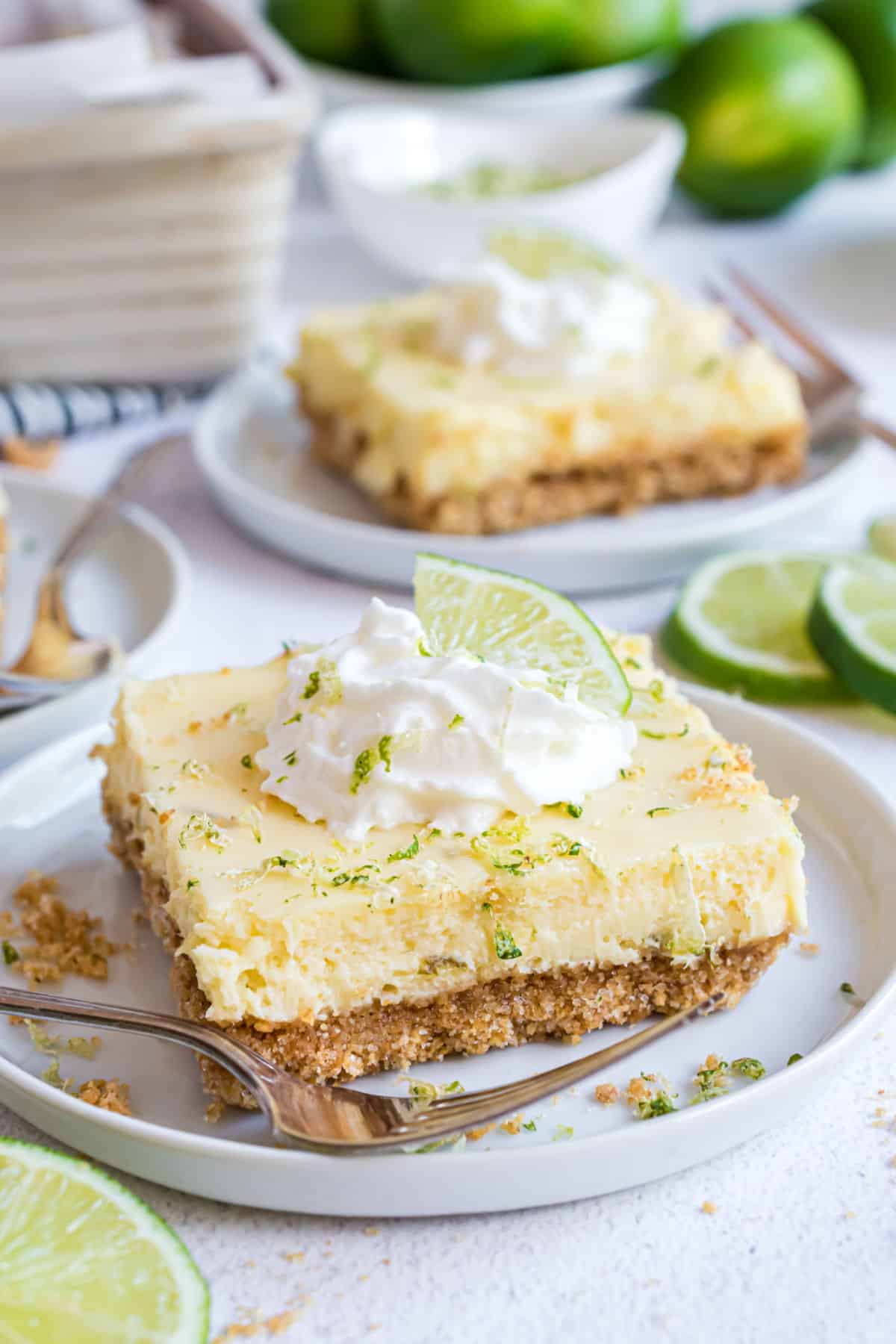 Key lime pie bars on white plates and garnished with whipped cream.