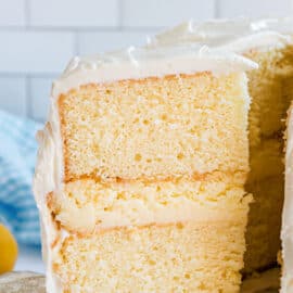 Slice of cake with two layers of lemon cake, cheesecake filling, and covered in frosting.