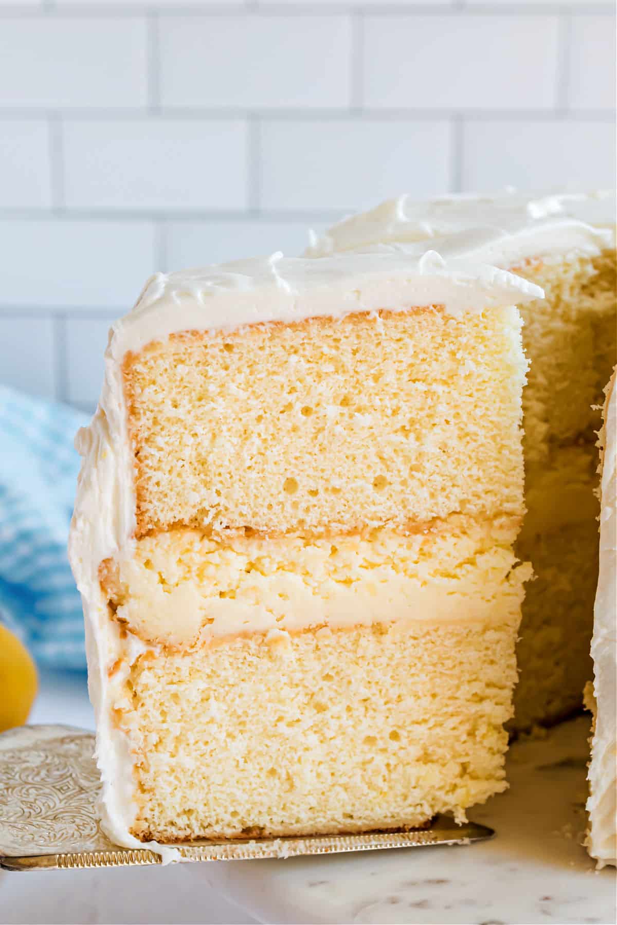 Slice of cake with two layers of lemon cake, cheesecake filling, and covered in frosting.