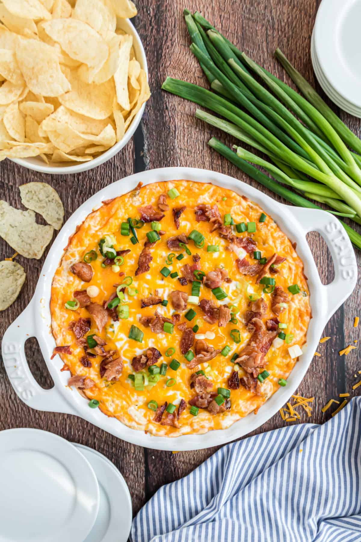 Warm potato chip dip in baking dish with scallions on the side.