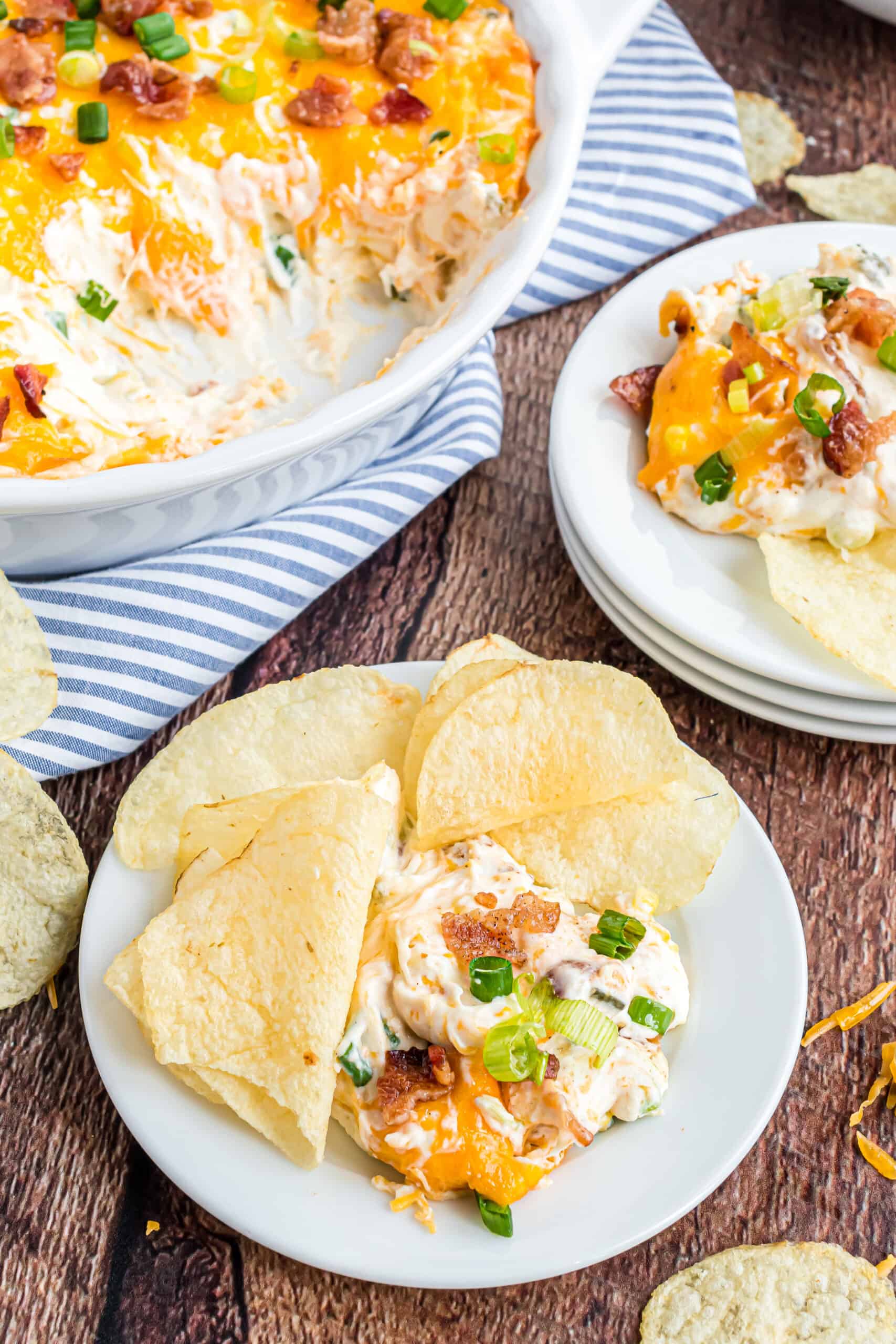Loaded baked potato dip on a white plate served with potato chips.